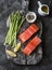 Raw organic salmon and young green asparagus on a rustic chopping board on a dark background, top view. Food ingredients