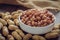 Raw peanuts in white bowl and peanut shell on wooden table