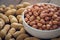 Raw peanuts in white bowl and peanut shell on wooden table