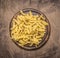 Raw penne pasta on a round cutting board on wooden rustic background top view close up