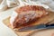 Raw piece of pork meat with fat rind rubbed with mustard and spices on a wooden kitchen board, ready prepared for the oven for a