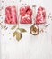 Raw pork fillet with spices and bay leaf in spoon on white wooden background