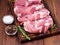Raw Pork Loin chops on a cutting board with herbs rosemary on dark wooden background, side view