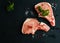 Raw pork steaks, crude cutlets with bones and fresh parsley on black stone background, top view