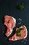 Raw pork steaks, crude cutlets with bones and fresh parsley on black stone background, top view