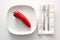 Raw red pointed sweet pepper on a white plate, cutlery and napkin beside on a bright background, healthy eating with vegetables or