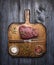 Raw ribeye steak on a cutting board with a fork, with rosemary salt and pepper on rustic wooden background, top view