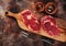 Raw ribeye steaks, spices and meat fork on wooden cutting board on a brown concrete background