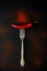 Raw ripe red chili pepper on fork with pepper peas and powder lying on dark wooden background. Top view. Flat lay