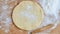 Raw round dough for pizza or pie with rolling pin and scattered flour on the wooden kitchen table. Baking background