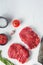 Raw rumpsteak, farm beef meat with seasonings, rosemary, garlic and butcher cleaver. White textured background. Top view vertical