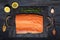 Raw salmon fillet on black slate plate and ingredients for making gravlax. Salt, sugar, lemon and rosemary in the background for