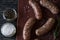 Raw sausages with salt, paper and rosemary on wooden surface.