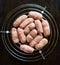 Raw sausages with spices on a round metal grill on a dark metal background with copy space for your text.