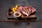 Raw split lamb ribs on a cutting board with in yellow tomatoes on a twig with multi-colored peppercorns peas on a wooden table