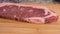 Raw striploin on wooden cutting board for preparation. side view of beef steak.