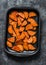 Raw sweet potato slices on a baking tray on a dark background, top view. Cooking baked sweet potatoes