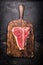 Raw T-bone steak on aged wooden cutting board on dark rust metal background, top view