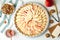 Raw traditional English apple pie in baking dish and ingredients on white table, flat lay