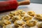 Raw traditional ravioli tortellini on wooden plate, grey table with flour