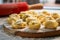 Raw traditional ravioli tortellini on wooden plate, grey table with flour