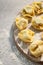 Raw traditional ravioli tortellini on wooden plate, grey table with flour