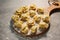 Raw traditional ravioli tortellini on wooden plate, grey table with flour