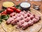 Raw turkey meat on skewers with garlic sauce bulgur seasoned tomatoes and herbs on a cutting board a wooden background close up