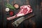 Raw uncooked black angus beef tomahawk steak on bone, and old butcher cleaver knife, with seasoning and herbs, on old dark  wooden