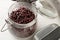 Raw, uncooked, dried adzuki red mung beans in glass storing jar with metal spoon on white wood table background