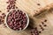 Raw, uncooked, dried adzuki red mung beans in small sieve on rustic wood table background with selective focus top view flat lay