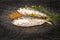 Raw uncooked Hilsa or terubok with mustard and green leaves on black board.