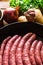 Raw uncooked sausages in iron cast pan, ingredients for hearty dinner vegetables potatoes, onions, garlic