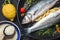 Raw uncooked seabass with rice, lemon, herbs and spices on black grilling iron pan over dark background