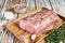 Raw Whole boneless pork loin meat with thyme and salt on rustic board. White wooden background. Top view