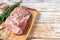 Raw Whole boneless pork loin meat with thyme and salt on rustic board. White wooden background. Top view. Copy space