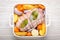 Raw wrapped rolled sliced pork in white casserole dish with potatoes, vegetables and herbs on rustic white wooden