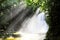 rays are coming from behind the waterfalls in the forest, with a body of water