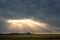 Rays of light penetrate through thick clouds during the ascension of the sun. Landscape: Field and dramatic dark sky during the s