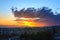 The rays of the setting sun break through a large cloud while sun goes down over the horizon. Golden blue evening sky over a small