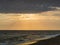 The rays of the sun break through the clouds over the beach at sunset. The dark waves of the sea roll over the sandy beach. A