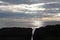 Rays of sunlight piercing clouds over coastline silhouetted rocks