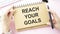 Reach your goals, the phrase is written on a notebook against a bright background. Business concept, strategy,