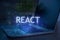 React inscription against laptop and code background. Technology concept. Learn react programming language, web development