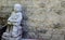 Reading book motion of Jizo little buddha statue sitting against old sandstone wall.