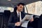 Reading latest news. Handsome young man in full suit reading a newspaper while sitting in the car