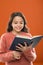 Reading practice for kids. Girl hold book read story over orange background. Child enjoy reading book. Book store