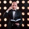 Reading your mind. Magician in black suit standing in the room with special lighting at backstage