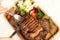 Ready grilled steak on a wooden plate, a portion of fresh salad. Children's hands cut meat.