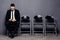 Ready for interview. Handsome man in formalwear holding phone and use it while sitting at the chair in waiting room